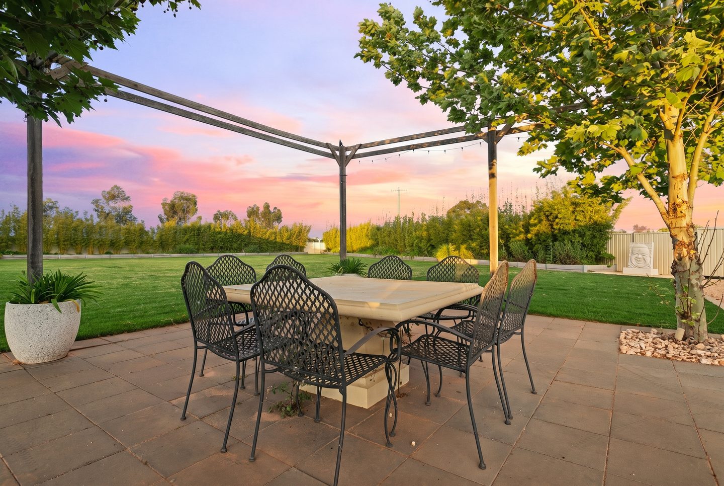 Paved garden terrace beneath an open pergola at dusk